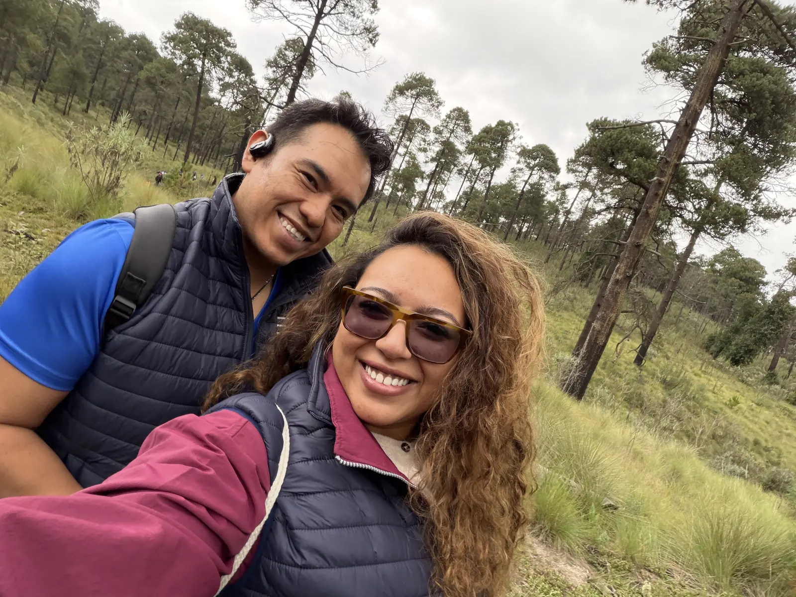 Dos integrantes del equipo sonriendo juntos, muy cerca el uno del otro, con el bosque de fondo