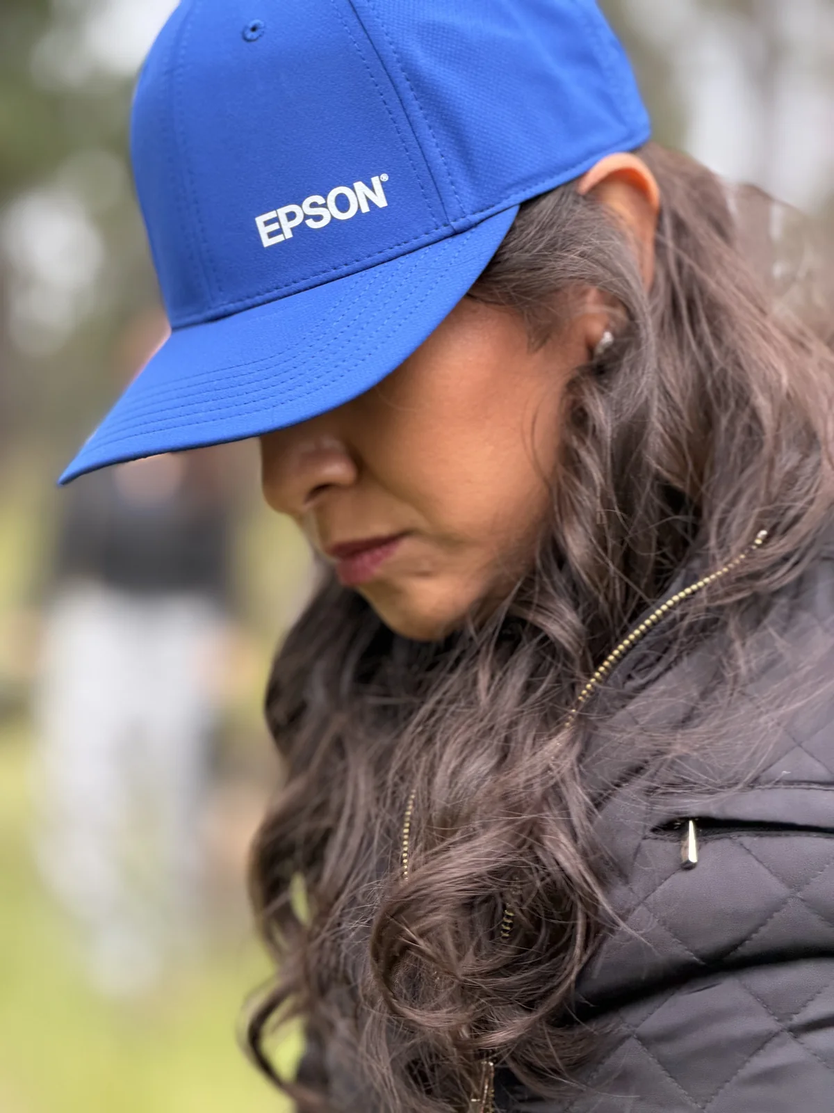 Retrato de perfil de una integrante del equipo con gorra Epson azul, mirada baja, en un momento de calma